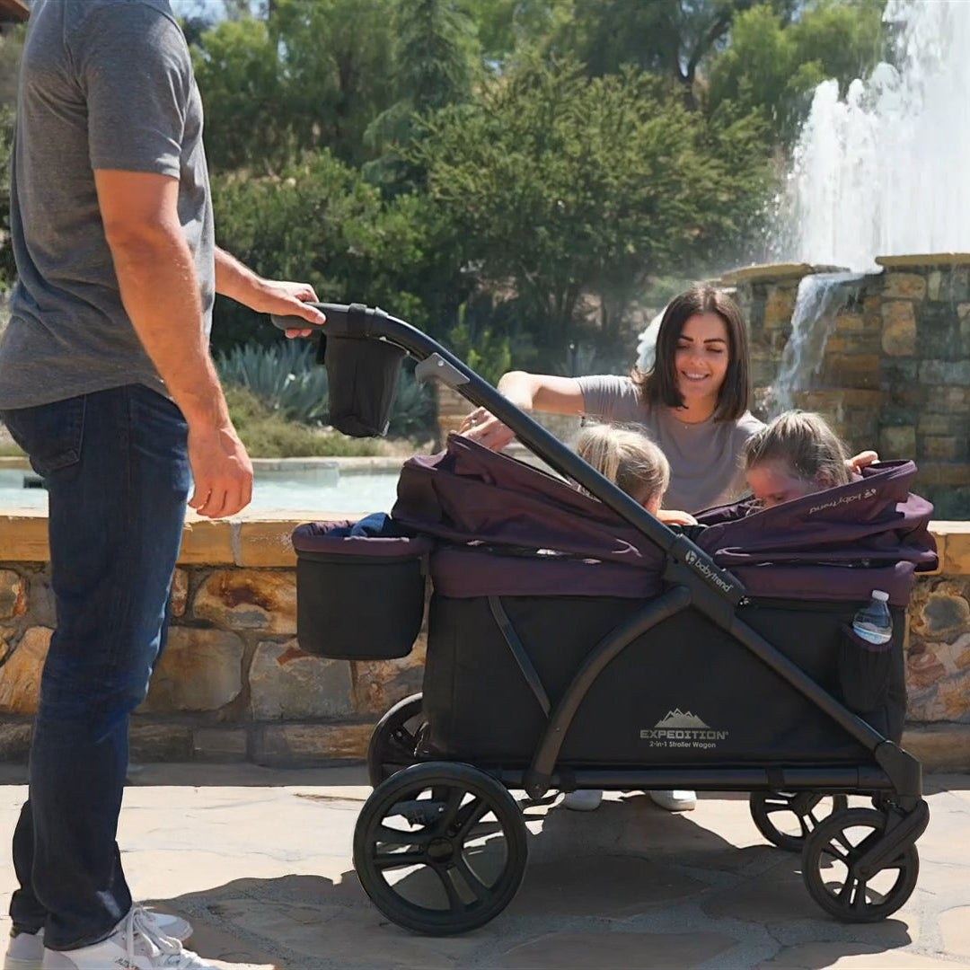 A dad taking two children for a walk in a Baby Trend Expedition stroller wagon at the park