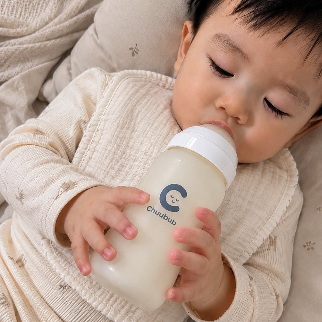 A baby holding and self-feeding from a Chuubub SiliGlass milk bottle