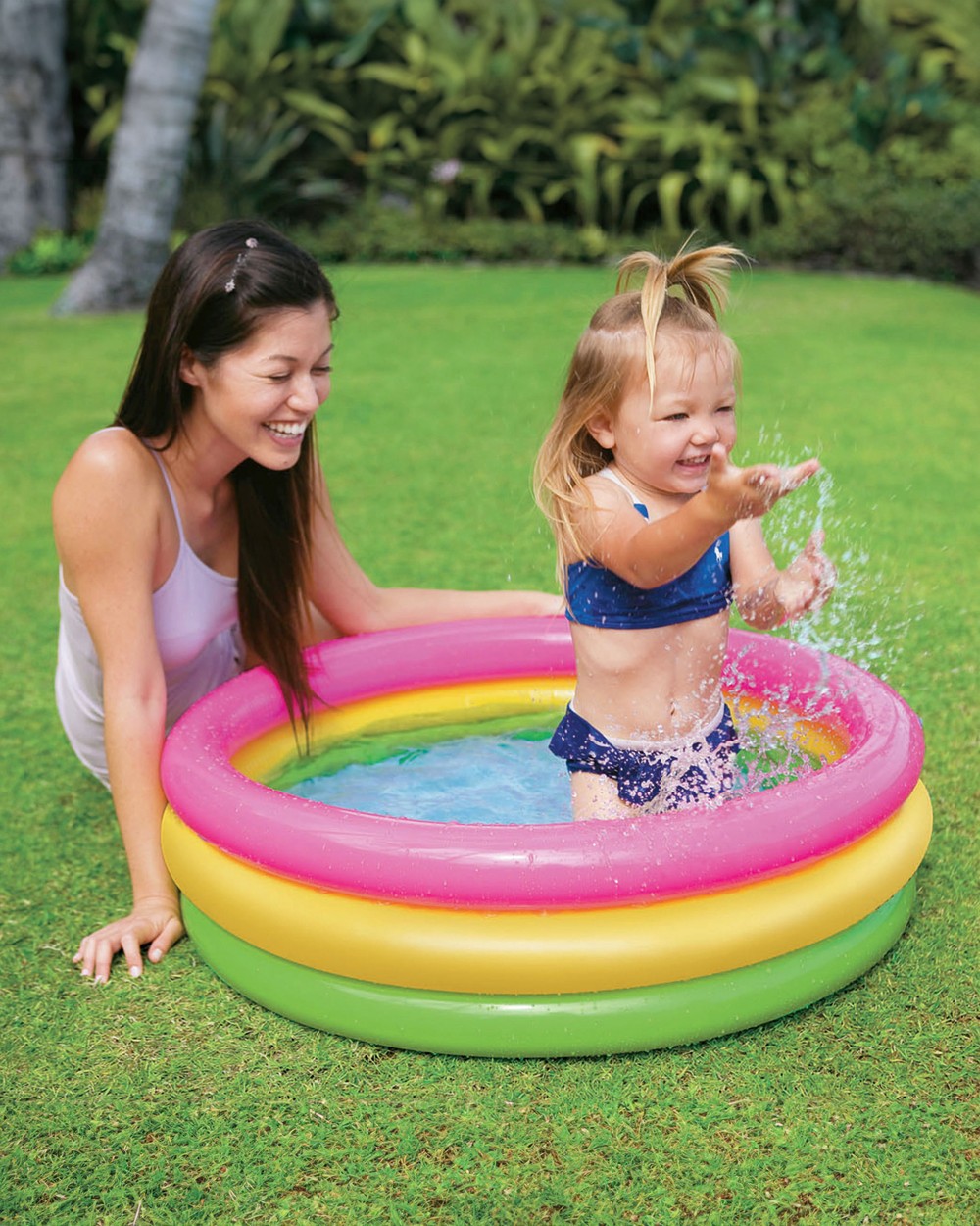 A toddler splashing happily in an Intex Sunset Glow paddling pool with mum