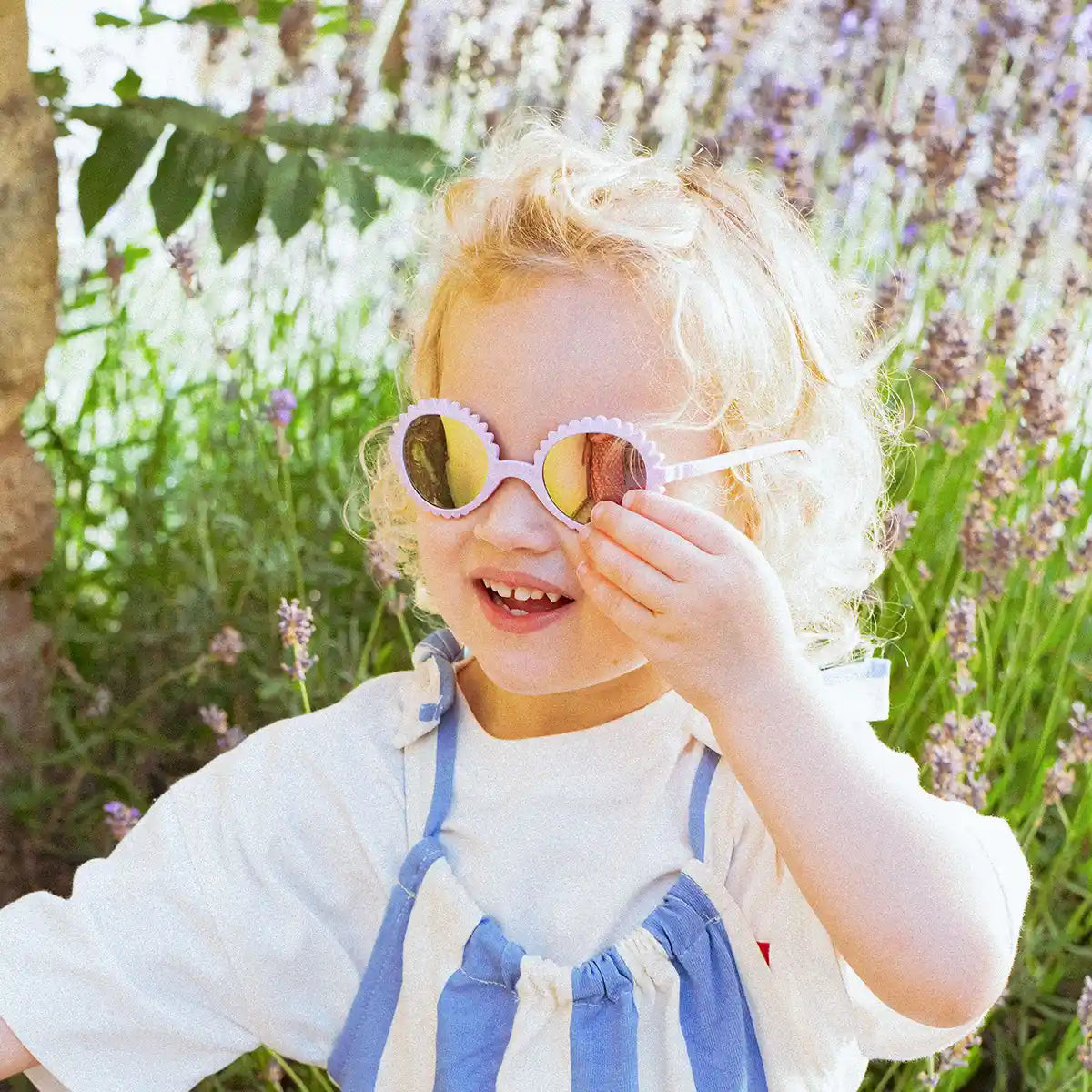 A laughing toddler in a lavender field wearing Ki ET LA flower-shaped sunglasses