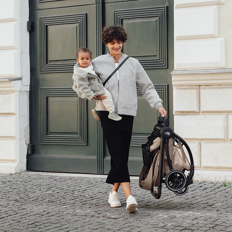 Parent carrying the folded Britax Rio and toddler
